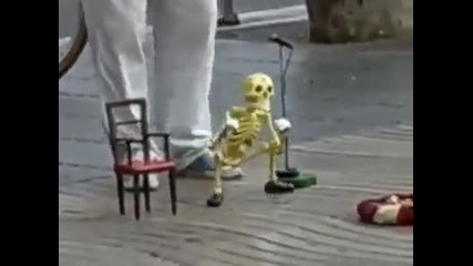 Уличен актьор управлява марионетка, малък скелет имитира пеене