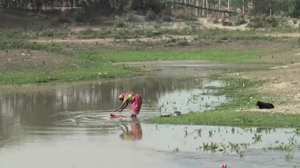 Жени перат дрехите си в мръсна вода 